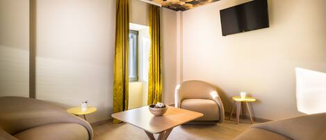 A modern room with a sofa, a small table with a bowl, a chair, and a TV mounted on the wall.