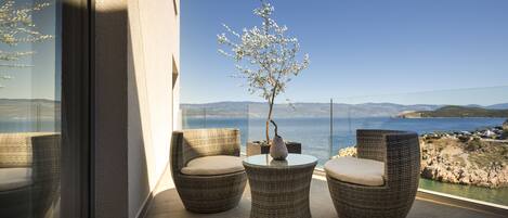 A balcony with wicker chairs and a table, overlooking a coastal landscape.