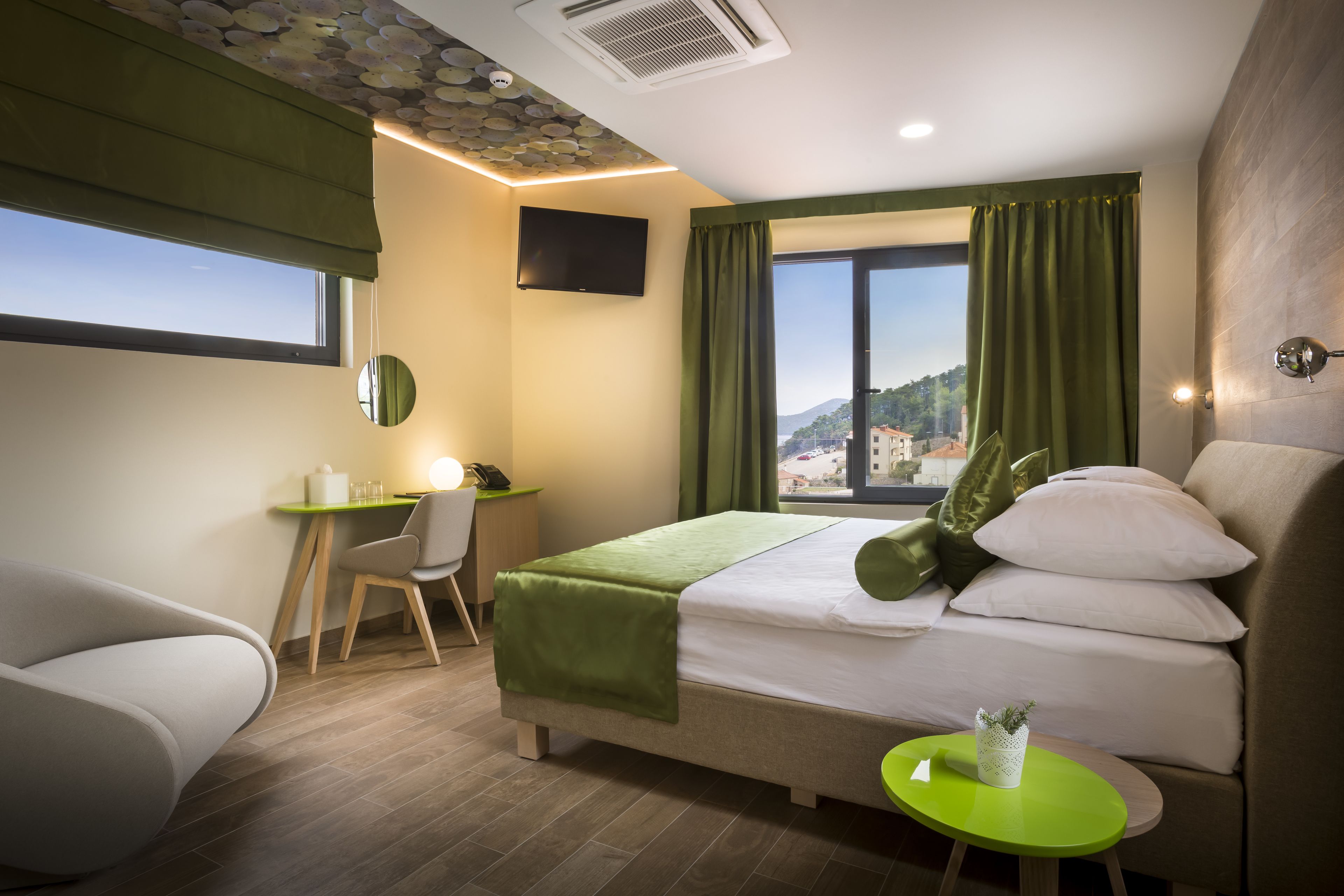 Una habitació d'hotel amb un llit, escriptori, cadira, taula petita, televisió i finestra amb cortines.