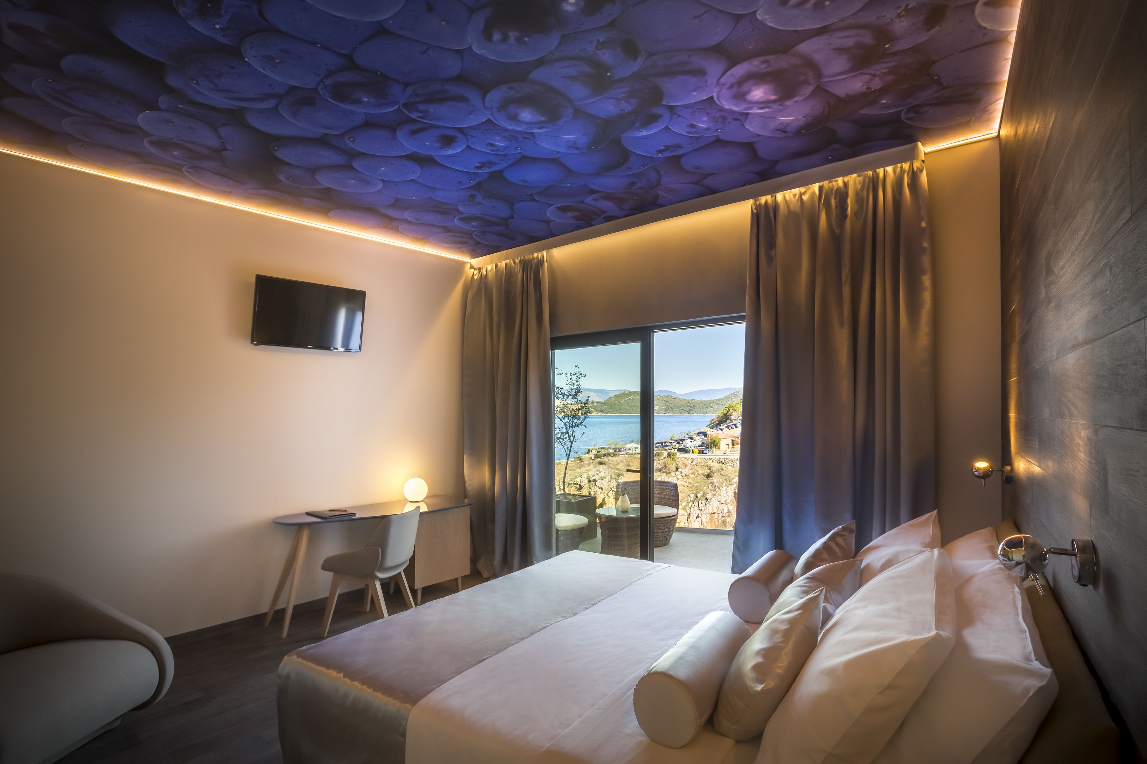 A hotel room with a bed, a desk, and a view of the sea.