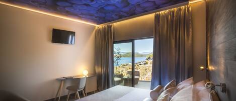 A hotel room with a bed, a desk, and a view of the sea.