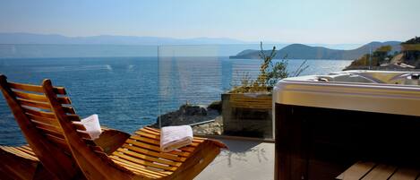Un fauteuil de relaxation en bois, une serviette, un jacuzzi et une vue sur la mer et les montagnes.
