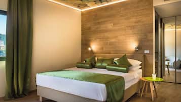 A modern hotel room with a wooden headboard, a neatly made bed with green bedding, a small round table, and a view of the outdoors through a window.