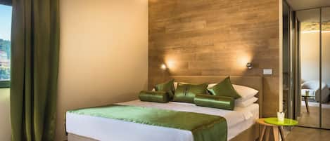 Una habitación de hotel moderna con cabecera de madera, cama bien hecha con ropa de cama verde, una pequeña mesa redonda y vistas al exterior a través de una ventana.