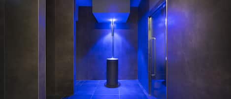 A hallway with a blue-lit floor, a cylindrical light fixture, and a door on the right.