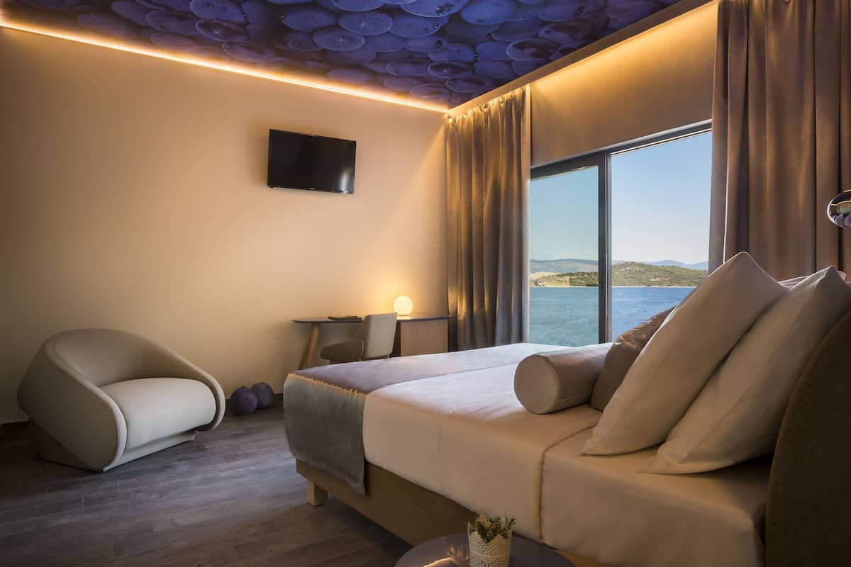 Una habitación de hotel moderna con una cama grande, un sofá, una televisión y vistas al mar.