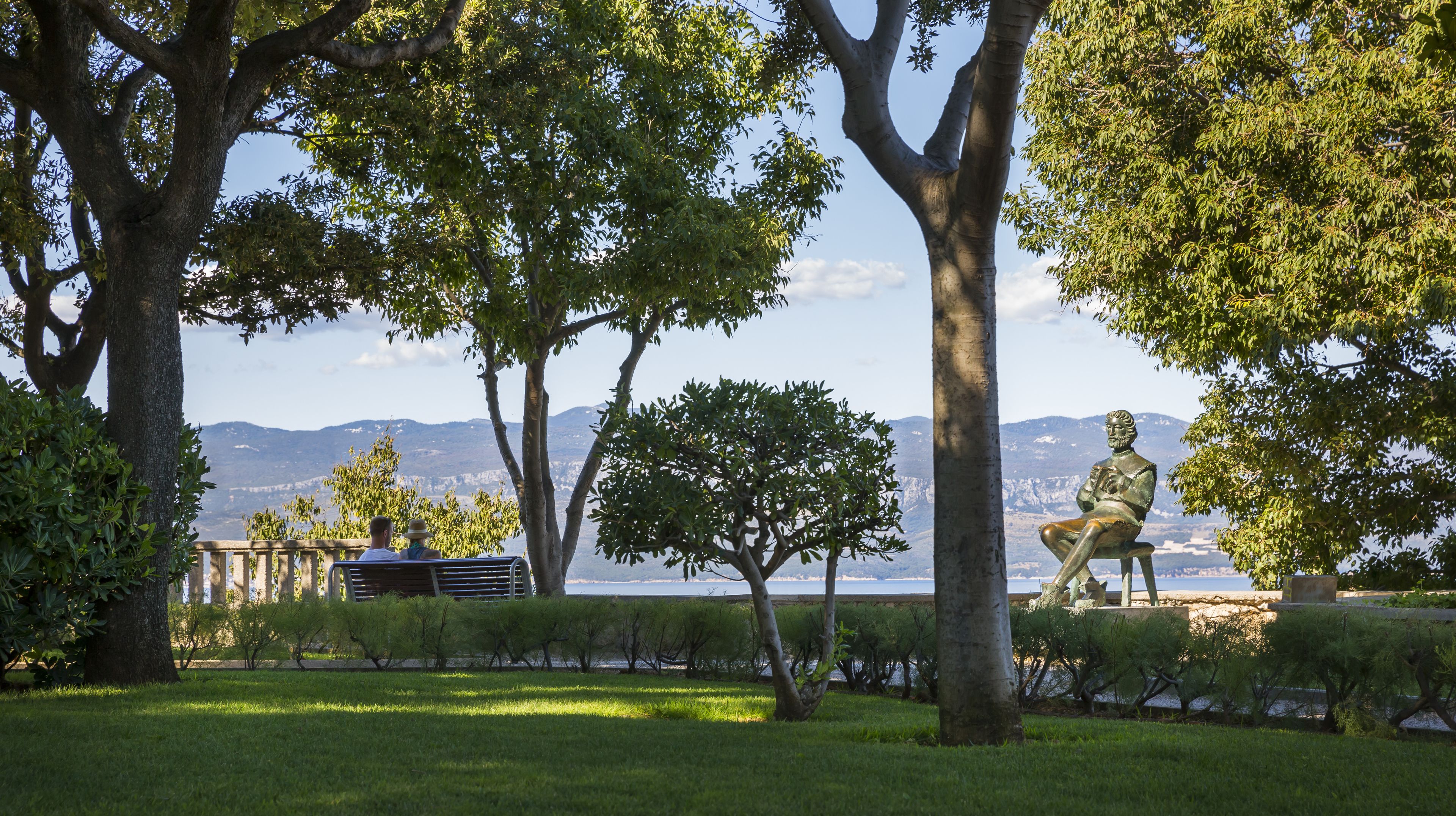 Un parc amb una estàtua, arbres i vista a les muntanyes.