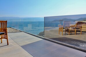 Una terraza con barandilla de vidrio que da a una playa y al mar.
