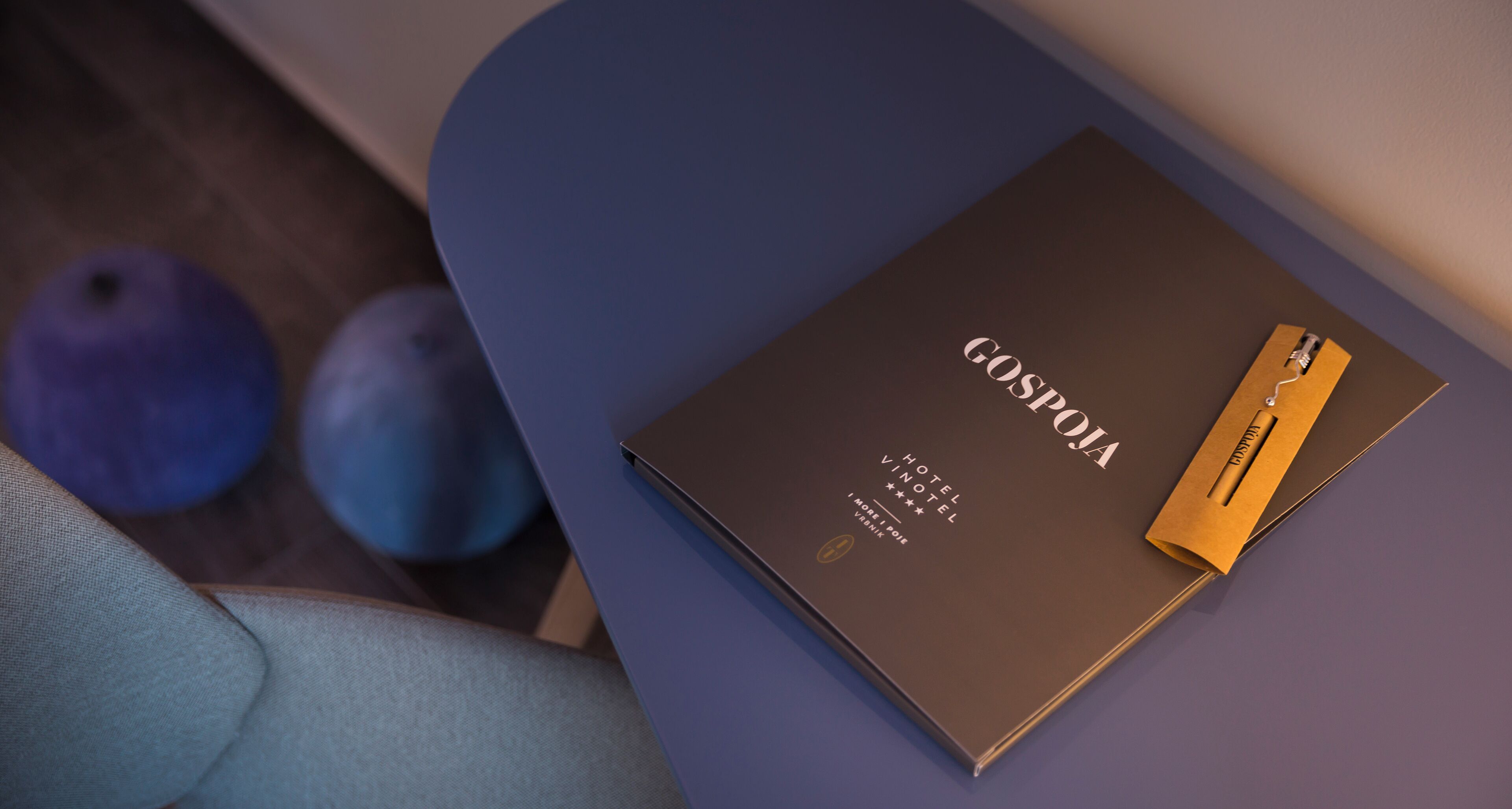 Un folleto marrón oscuro titulado 'GOSPÓJA HOTEL VINTEL' con un bolígrafo dorado encima, sobre una superficie azul.