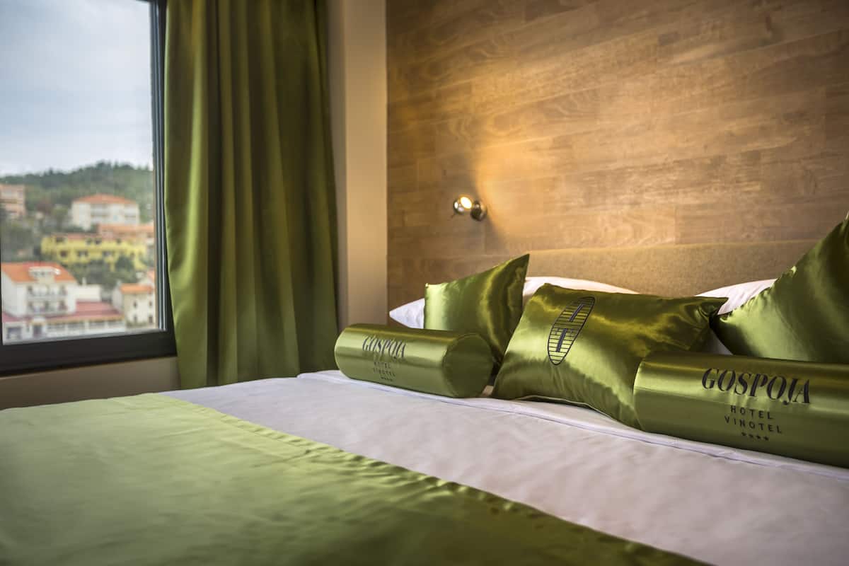 Habitación de hotel con cama, cortinas verdes y vistas a edificios.
