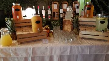 Una estación de bebidas con varios dispensadores y vasos, rodeada de cajas de madera y frutas tropicales.