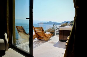 Un balcon avec deux chaises en bois, une petite table et une vue sur la mer et les montagnes lointaines.