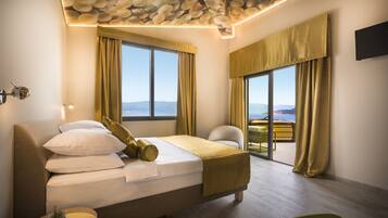 A modern hotel room with a large bed, a view of the mountains, and a balcony with yellow curtains.