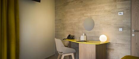 A hotel room with a wooden accent wall, a desk with a telephone and a lamp, a chair, and a bed.