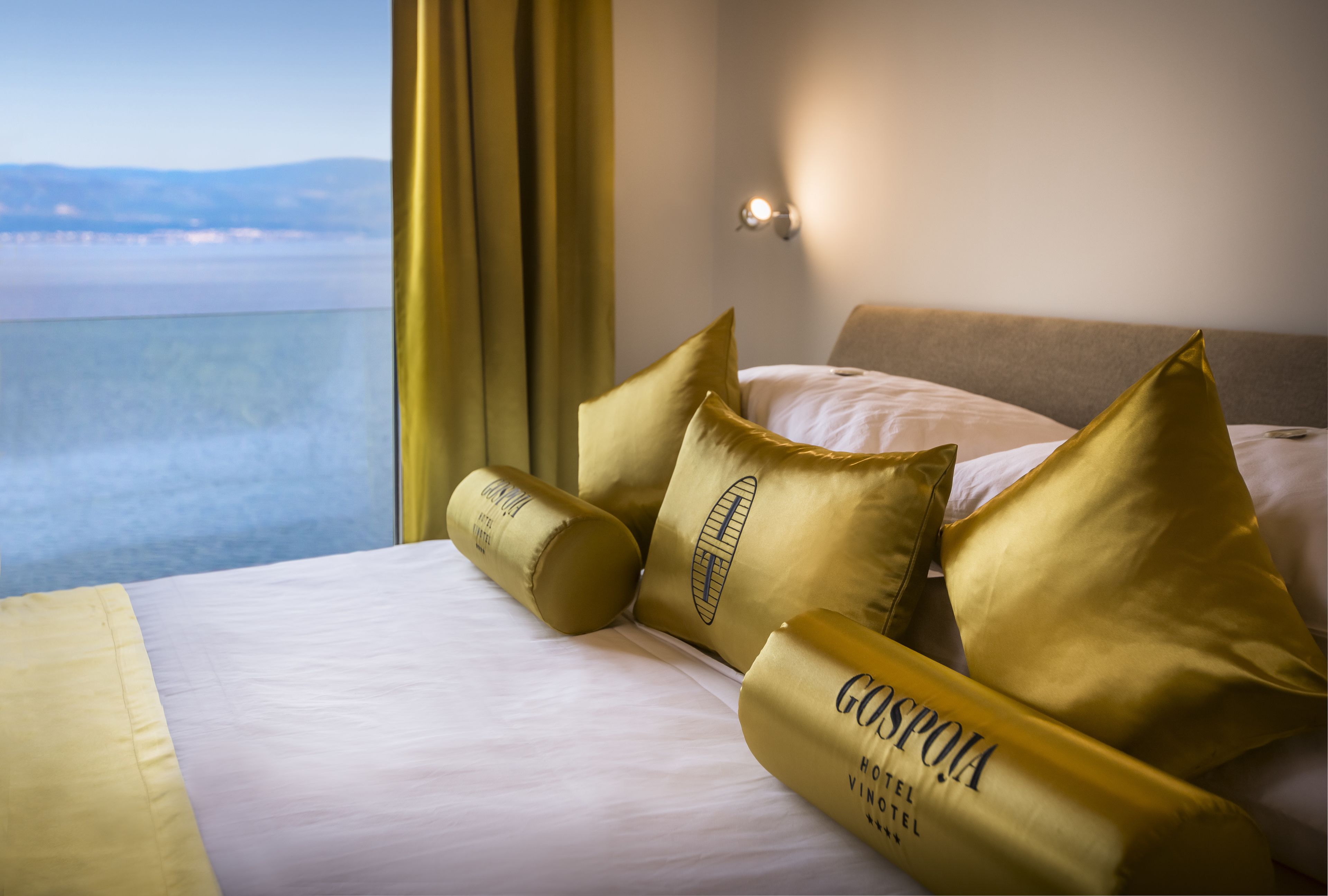 Una habitación de hotel con una cama, almohadas doradas y vista al mar.