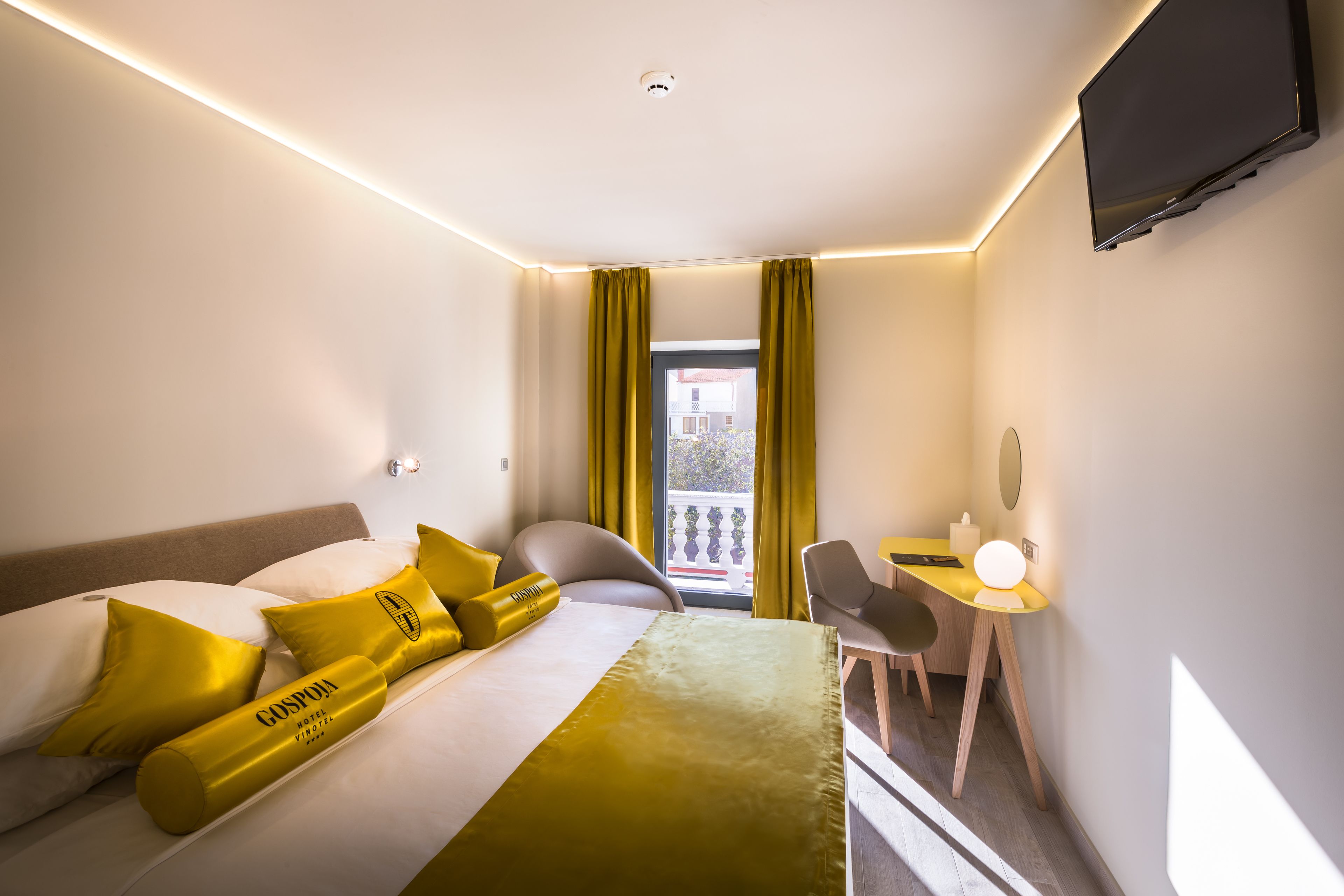 A hotel room with a bed, a desk, a chair, and a television.