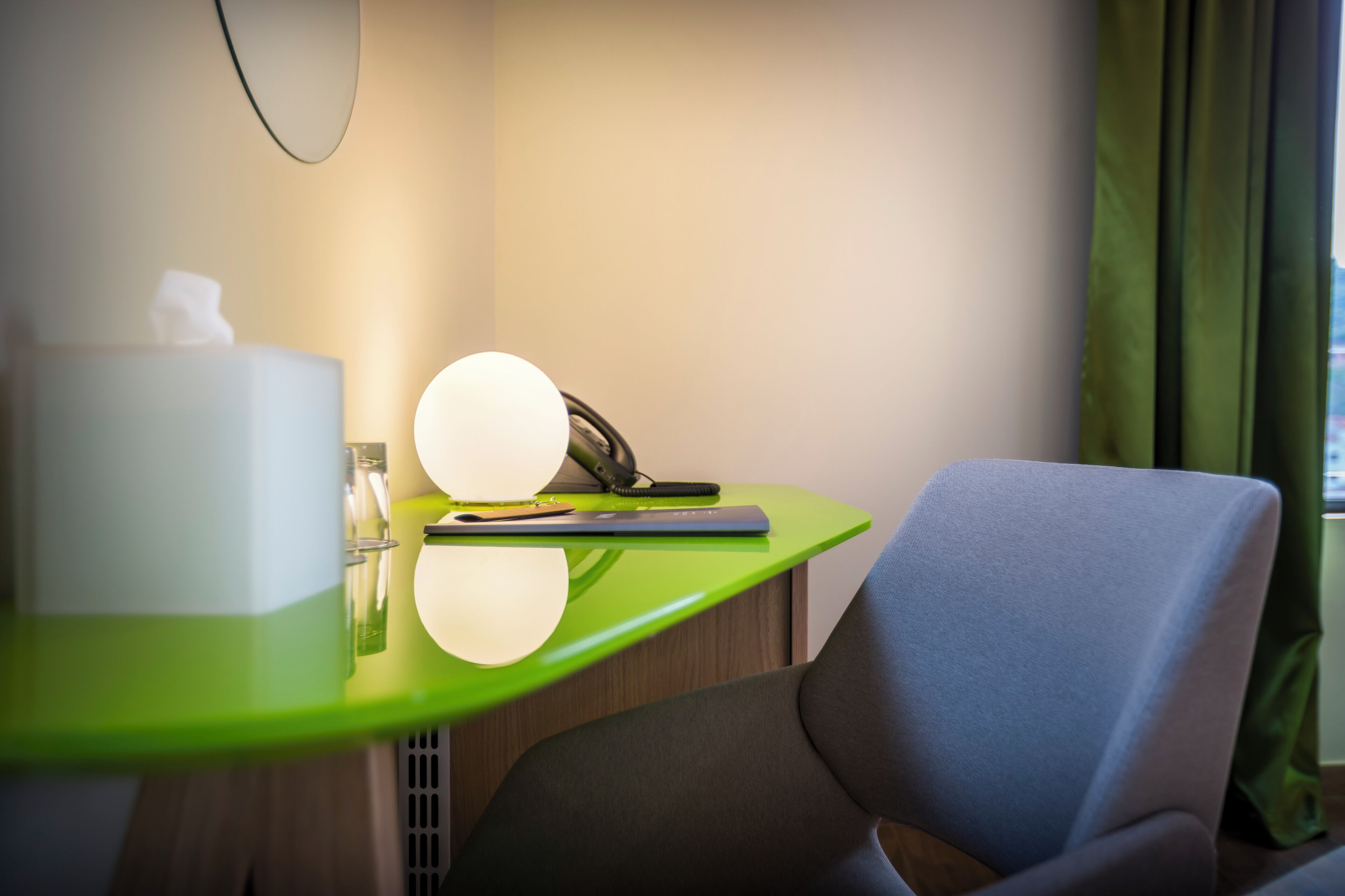 Une chambre d’hôtel avec un bureau vert, une lampe, une boîte de mouchoirs et une chaise.