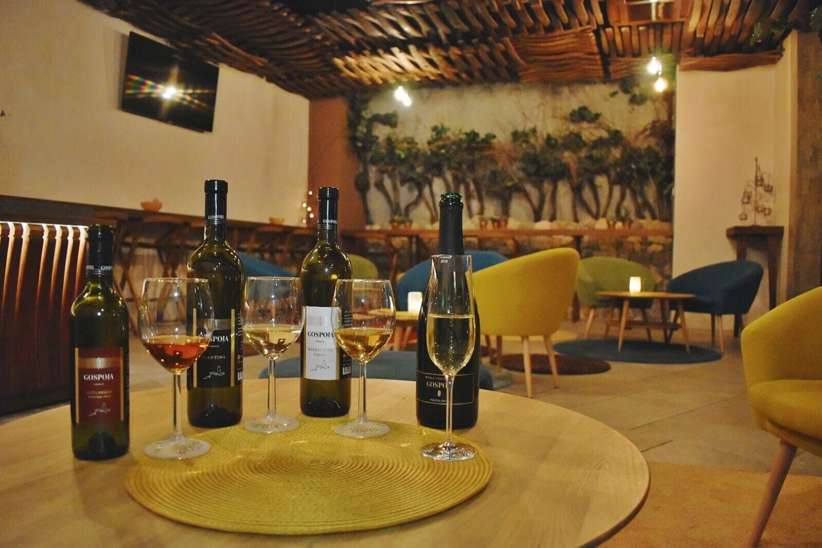 A restaurant interior with a round table set for four, featuring wine bottles and glasses.