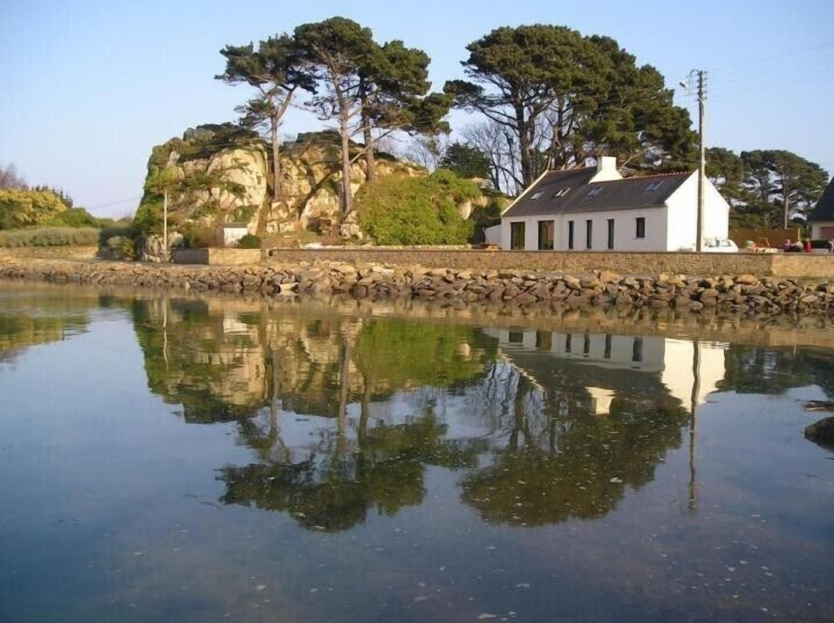A coastal building with a stone wall and a calm water body reflecting its structure.