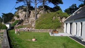 A grassy yard with a small garden, a stone wall, and a building with a sloped roof.