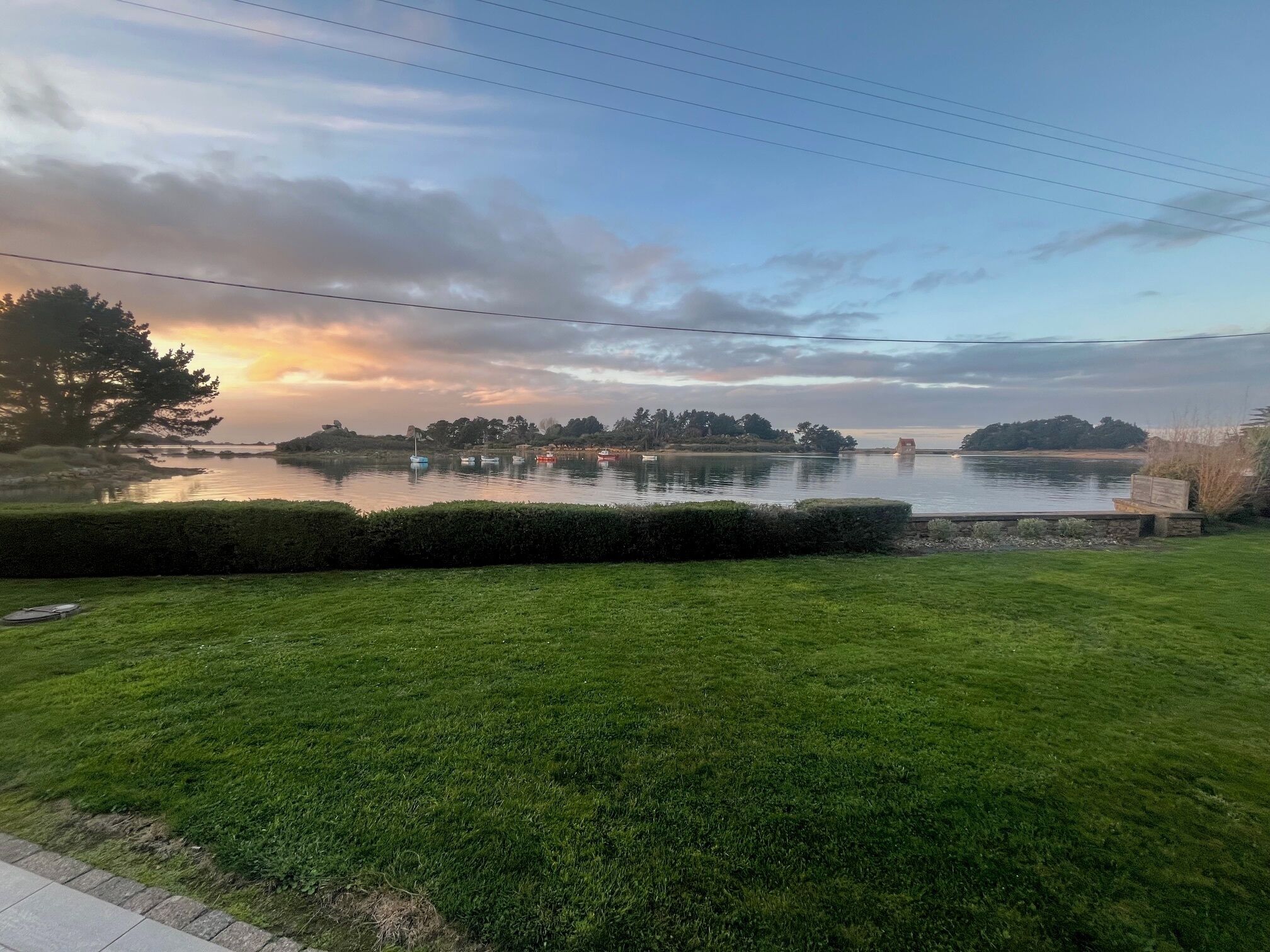 En rogivande utsikt över en sjö med båtar, en välskött gräsmatta och en avlägsen strand med träd och byggnader.