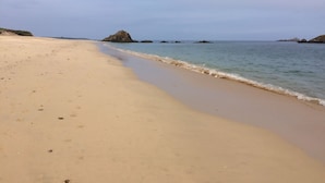 A wide sandy beach with gentle waves and rocky outcrops in the distance.