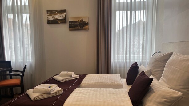 A hotel room with a bed, a chair, a desk, and curtains. - sevenDays Hotel BoardingHouse (Karlsruhe)