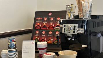 Un espace dédié au café, comprenant une machine à café, des tasses et un présentoir avec différentes sortes de café en boîte.