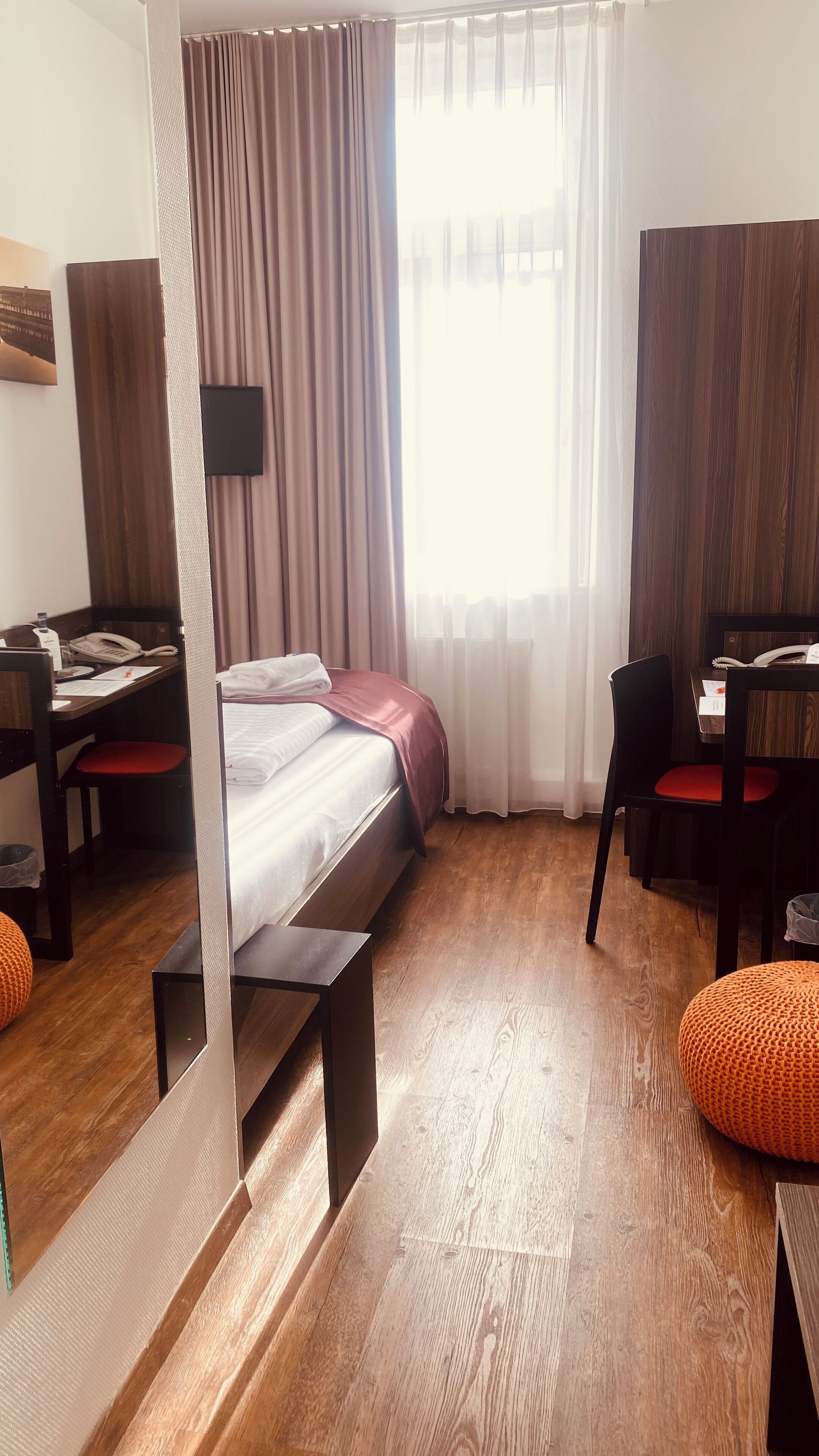 A hotel room with a bed, a desk, a chair, a small table, and a window with curtains.