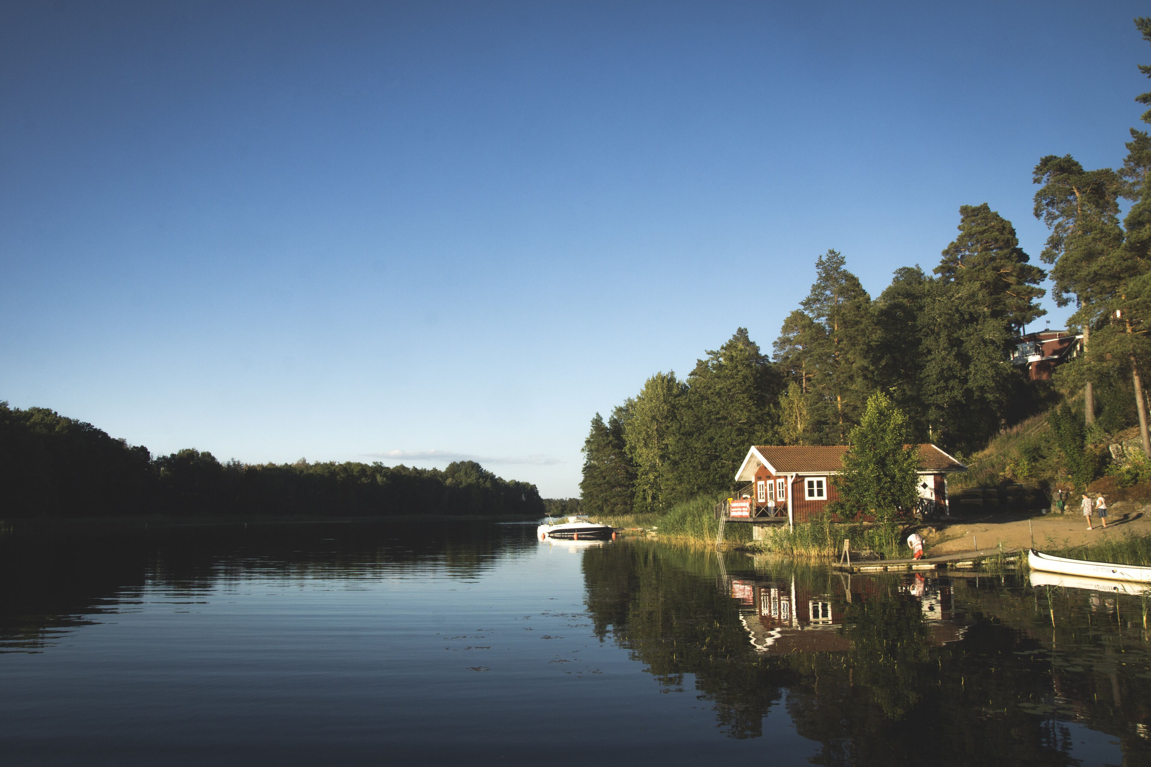 Ein ruhiger See mit einem Haus am Ufer, einem Steg und einem Boot.