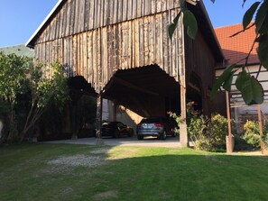 A rustic barn with a covered entrance, a parked car, and surrounding greenery.