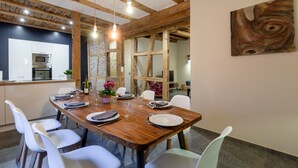 Un coin repas avec une table en bois dressée pour quatre personnes, des chaises blanches et une cuisine en arrière-plan.