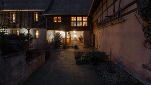 Une maison traditionnelle avec un chemin de gravier menant à l’entrée, entourée de végétation et d’un mur de pierre.