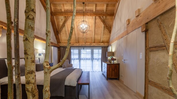 Une chambre avec un plafond en bois, une grande fenêtre et un lit avec une banquette.
