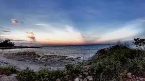 A coastal landscape with a rocky shoreline, vegetation, and a view of the sea under a cloudy sky. - 9 Huts on a Hill (Kudat)