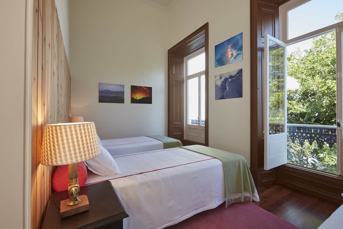 Ein Hotelzimmer mit zwei Betten, einem Fenster mit Blick auf Bäume und einem Kunstwerk an der Wand.