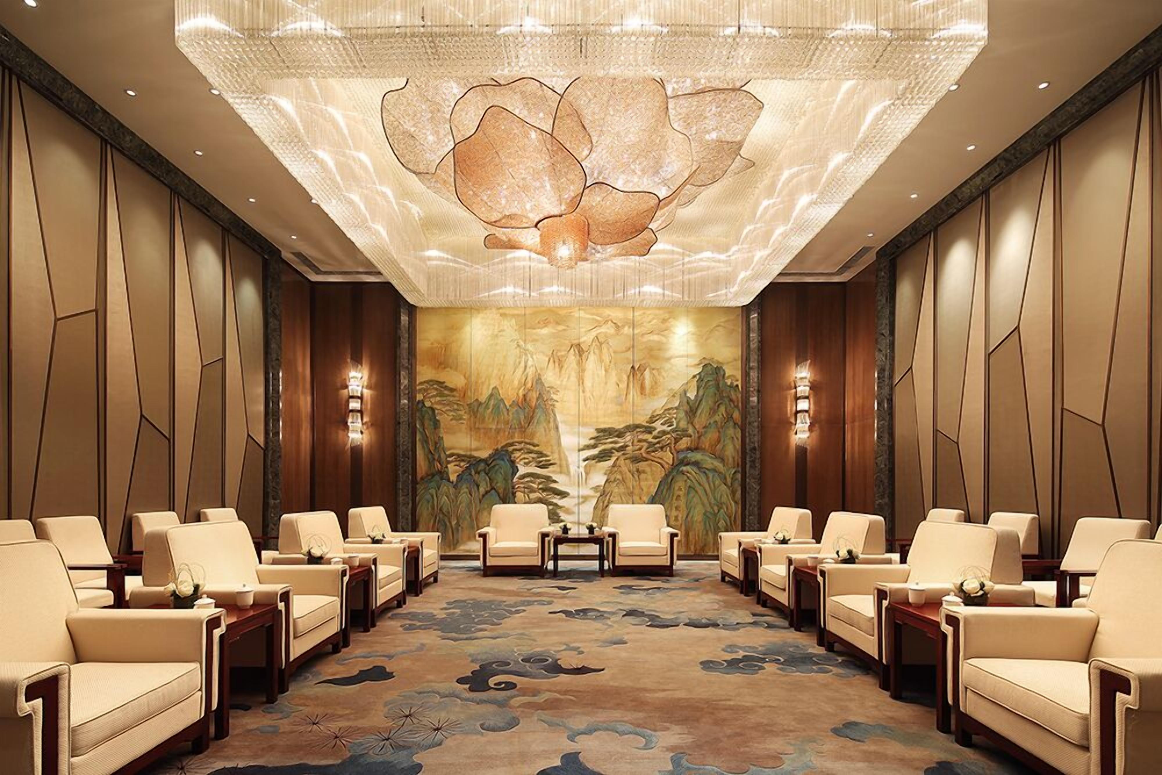 Un hall d’entrée spacieux avec un espace salon central, une grande fresque murale et un lustre moderne.
