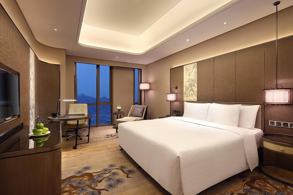 Habitación de hotel con una cama grande, un escritorio con silla, televisor y vista al mar.