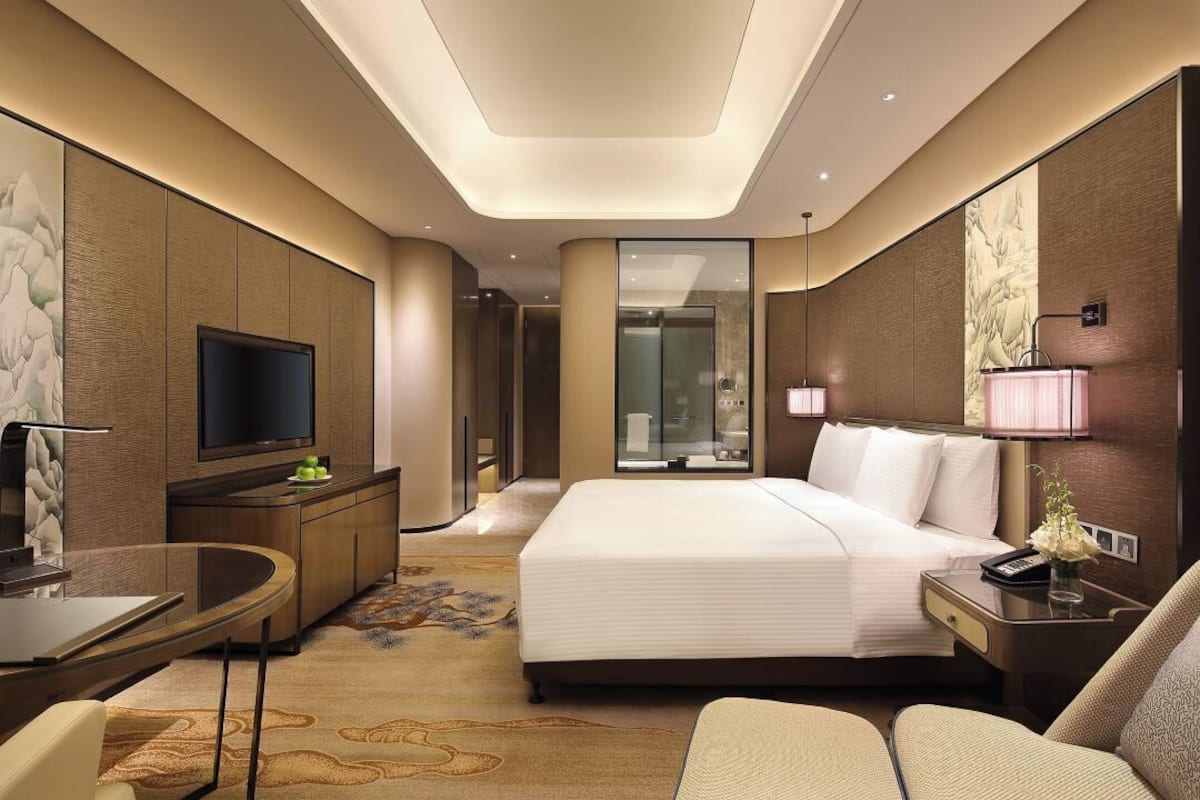 Una habitación de hotel moderna con una cama grande, un televisor de pantalla plana, un escritorio y un espacio de descanso.