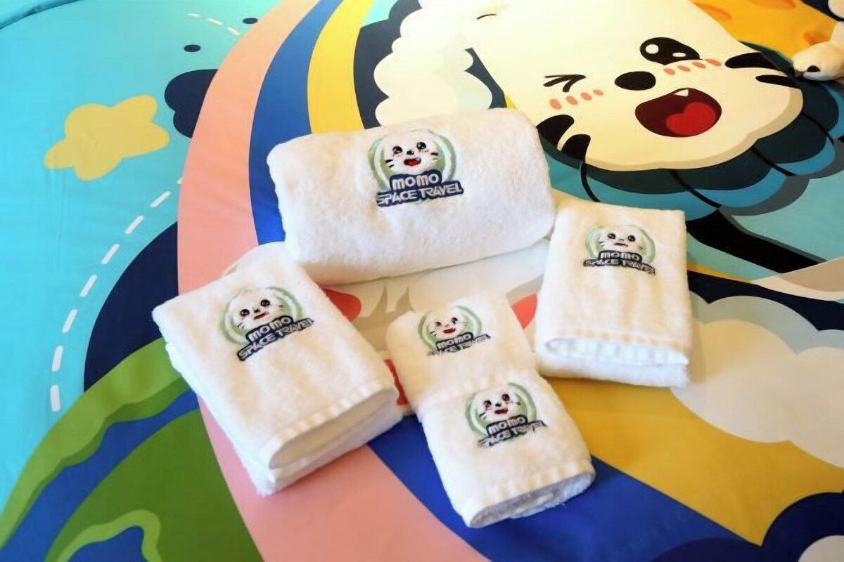 Four white towels with a cartoon character logo on a colorful bedspread.