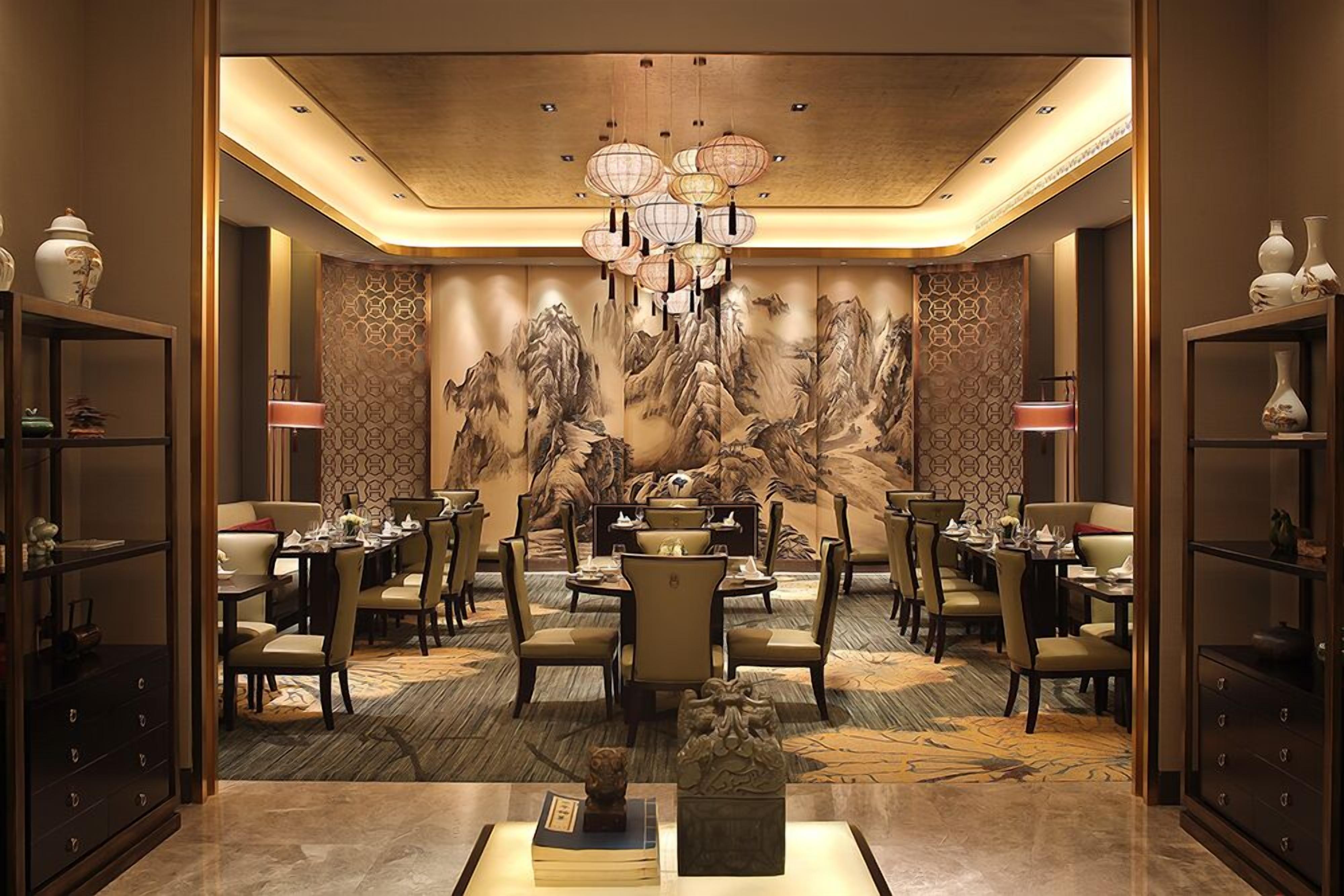 A dining area with round tables, chairs, and a central chandelier.