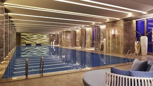 A modern indoor swimming pool with a clear water surface, surrounded by stone walls and a seating area with cushions. - Wanda Realm Taian (Tai'an)