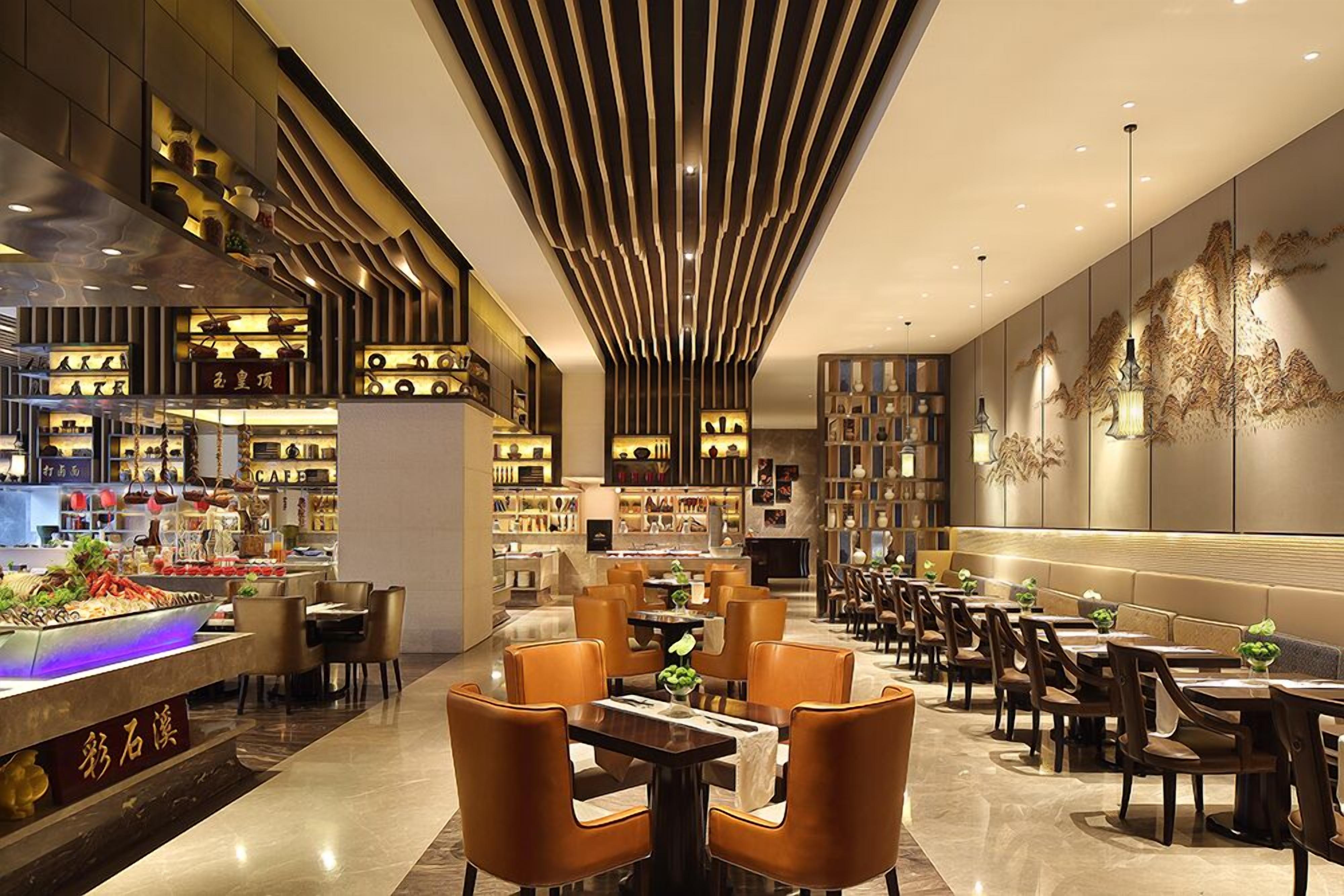 Interior moderno de restaurante con zona de comedor central, barra con exhibición de alimentos y pared con elementos decorativos.