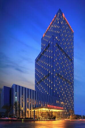 A high-rise hotel with a modern facade, illuminated windows, and a prominent entrance with signage. - Wanda Realm Taian (Tai'an)