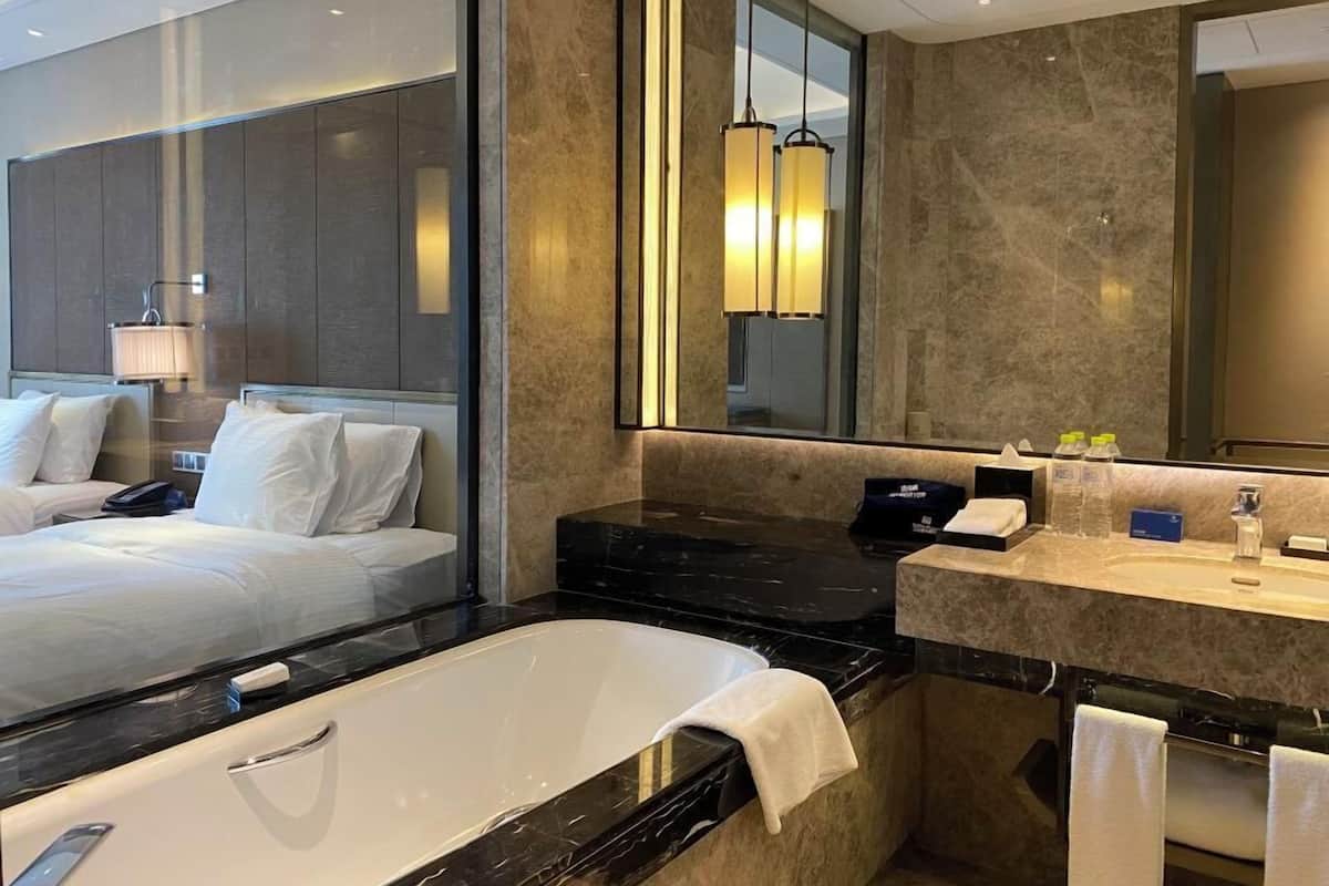 Habitación de hotel con una cama grande, un baño separado con bañera, un tocador con espejo y un espejo grande sobre el tocador.
