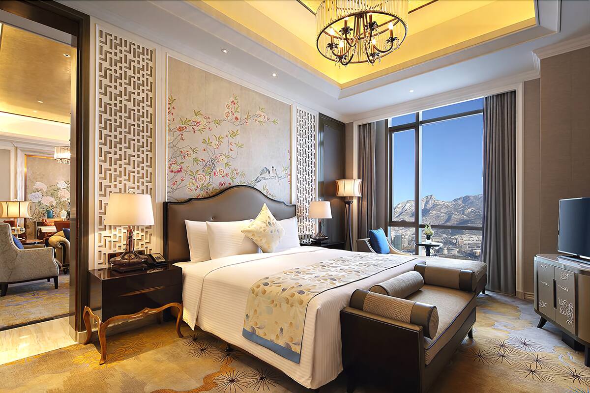 Habitación de hotel con una cama grande, un rincón de descanso, televisor y vistas a las montañas.
