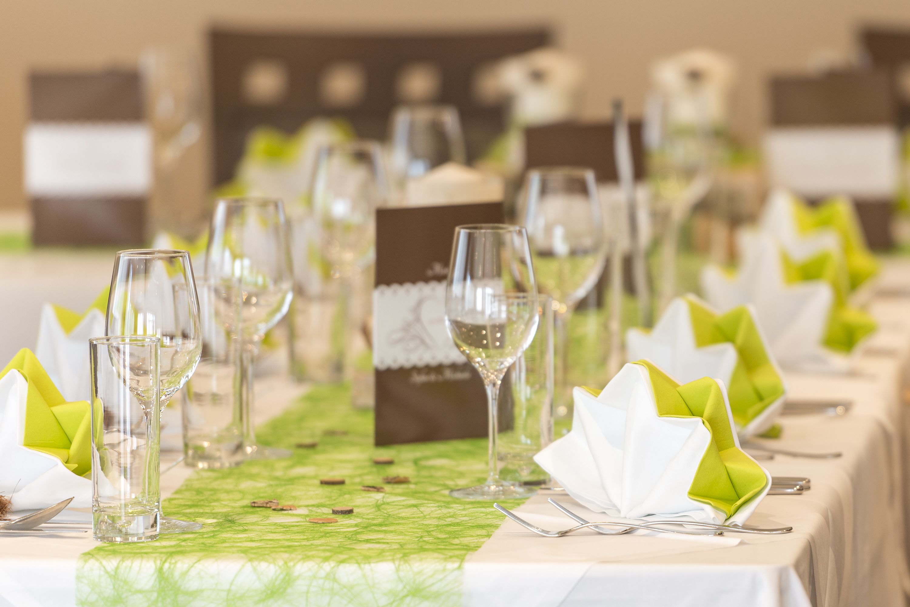 A table set with clear glasses, white napkins, and green centerpieces.