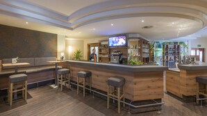 Eine Bar mit hölzernen Barhocker, einer Theke und einem Fernsehbildschirm.