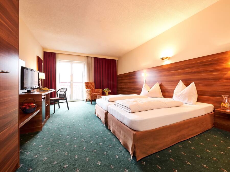Une chambre d’hôtel avec une tête de lit en bois, un bureau avec une télévision, une chaise et un lit avec des oreillers.