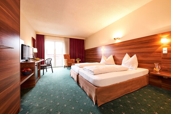 Habitación de hotel con cabecera de madera, un escritorio con televisor, una silla y una cama con almohadas.